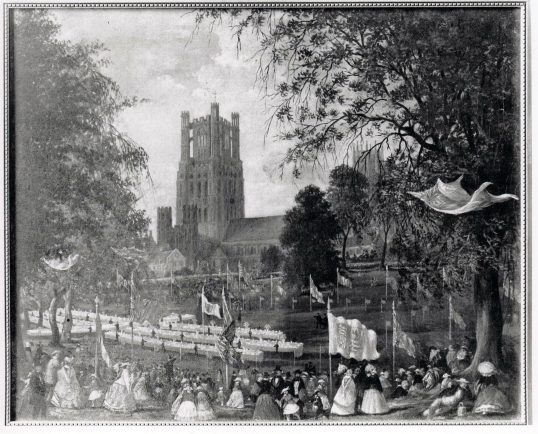 Celebration in the Dean's Meadow 1863 with the cathedral in the background, flags flying and ladies in period dresses. 
