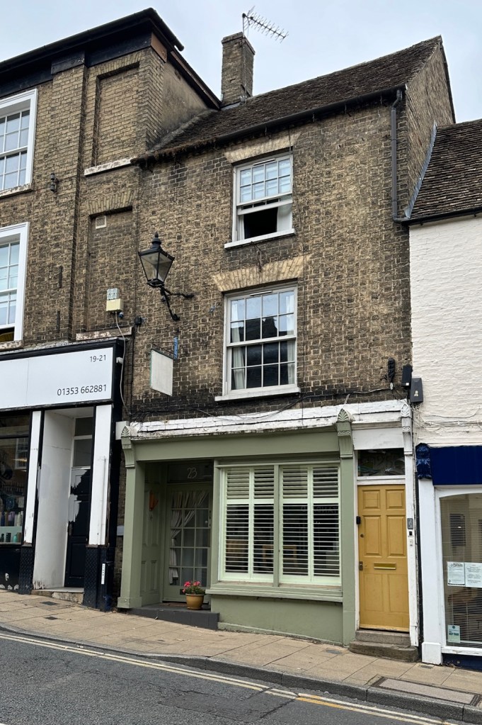 23 Fore Hill, Ely. 2024, a narrow three storey building with a shop entrance and main front door beside it, a Georgian sash window on each floor above.